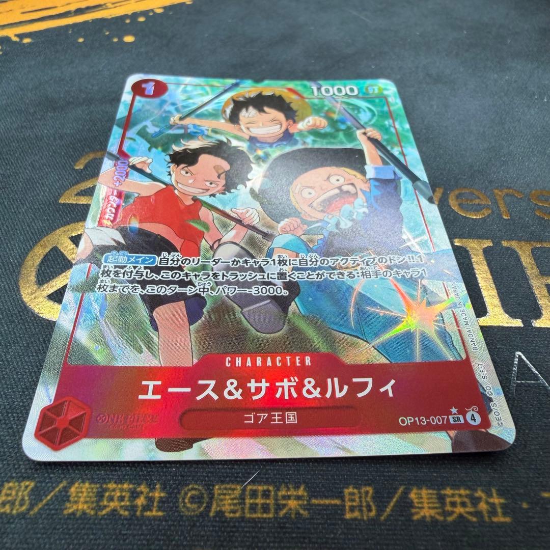 One Piece OP13-007 SR parallel figure card showing Ace, Sabo, and Luffy in PSA sleeve