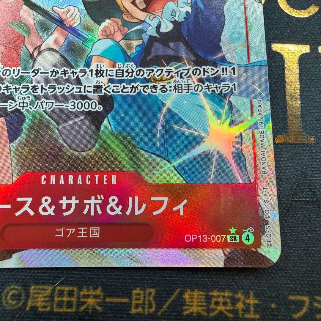 One Piece OP13-007 SR parallel figure card showing Ace, Sabo, and Luffy in PSA sleeve