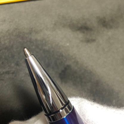 Blue metal-bodied Brand Crossball ballpoint pen with silver tip and visible scratch on glossy surface