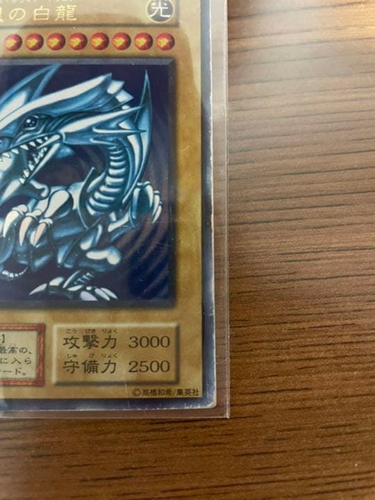 Yu-Gi-Oh Blue-Eyes White Dragon early edition trading card with visible wear and protective sleeve