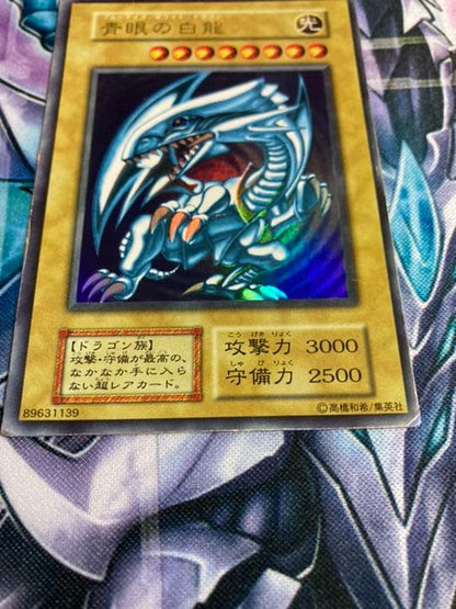 Sony Ultra Rare Blue-Eyes White Dragon Yu-Gi-Oh card showing light edge wear and scratch damage