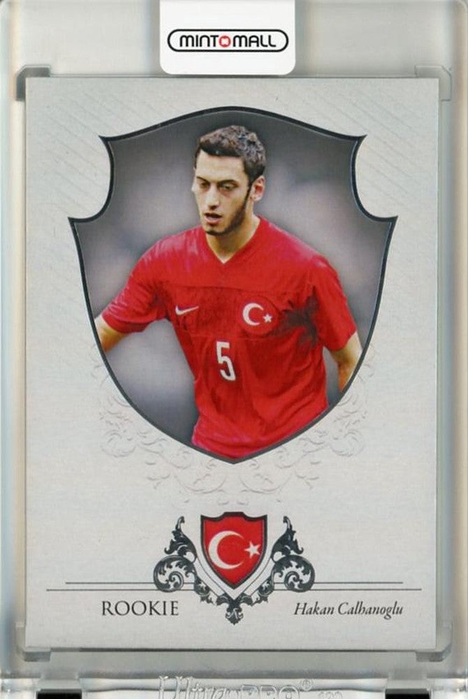 2016 Futera World Football Unique Hakan Calhanoglu Silver RC card with serial number 9102/21 showing initial damage