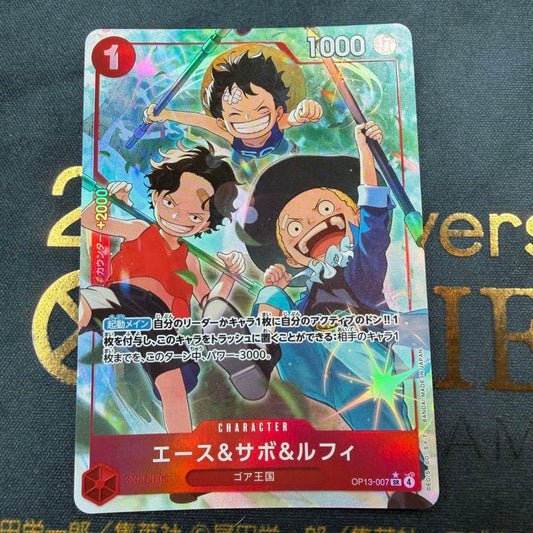 One Piece OP13-007 SR parallel figure card showing Ace, Sabo, and Luffy in PSA sleeve
