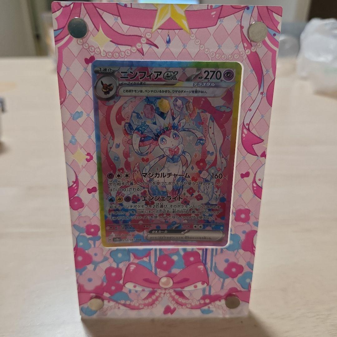 Ninfiaex Sar Scarlet & Violet card with display stand included, shown in protective sleeve