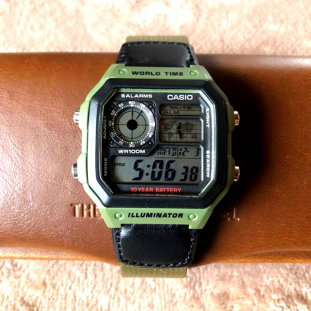 Casio AE-1200WH-1B digital watch with khaki case and black leather khaki nylon cross band showing world time display