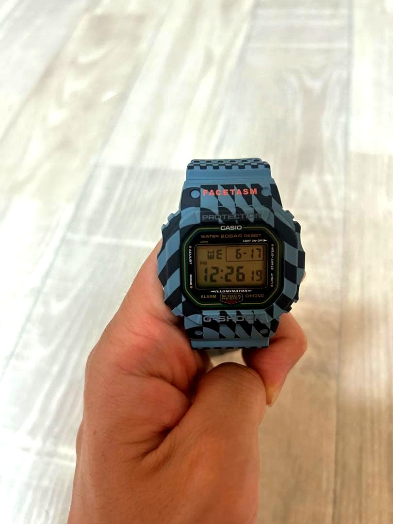 Casio G-Shock Facetasm DW-5600 digital watch with blue-gray and black checkerboard pattern and orange keeper