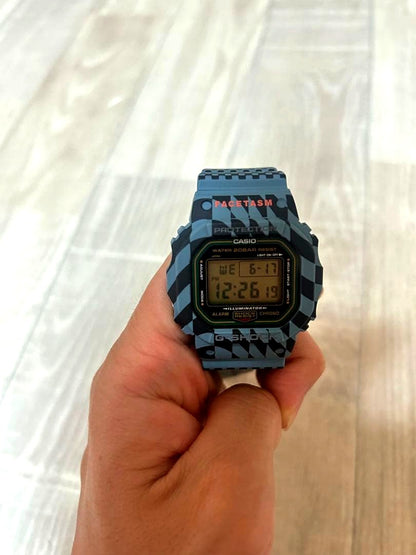 Casio G-Shock Facetasm DW-5600 digital watch with blue-gray and black checkerboard pattern and orange keeper