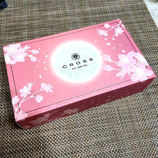 Cross Sakura pink ballpoint pen with cherry blossom pattern next to its cherry blossom design and black box packaging