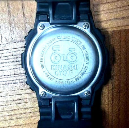 Casio G-Shock DW-5600BB-1J black watch with Kinashi Cycle logo on dial, showing front view