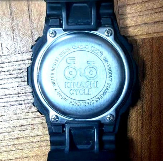 Casio G-Shock DW-5600BB-1J black watch with Kinashi Cycle logo on dial, showing front view