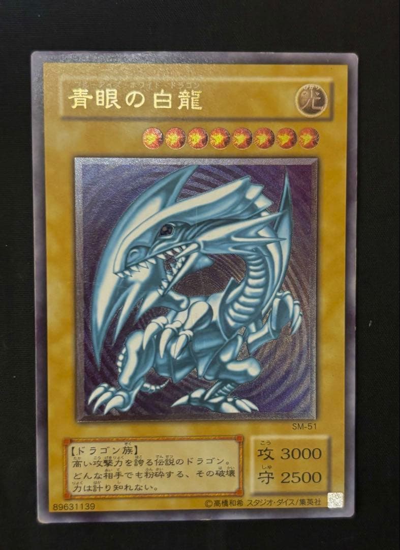 Used Yugioh Blue-Eyes White Dragon Ultra Rare SM-51 trading card from Japan with visible scratches and damage