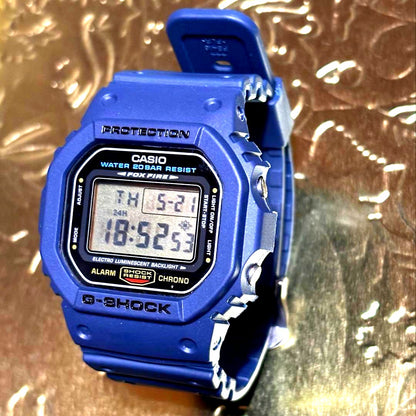 Casio G-Shock DW-5600E watch body with navy replacement bezel and belt showing backlight reading SHINOBU