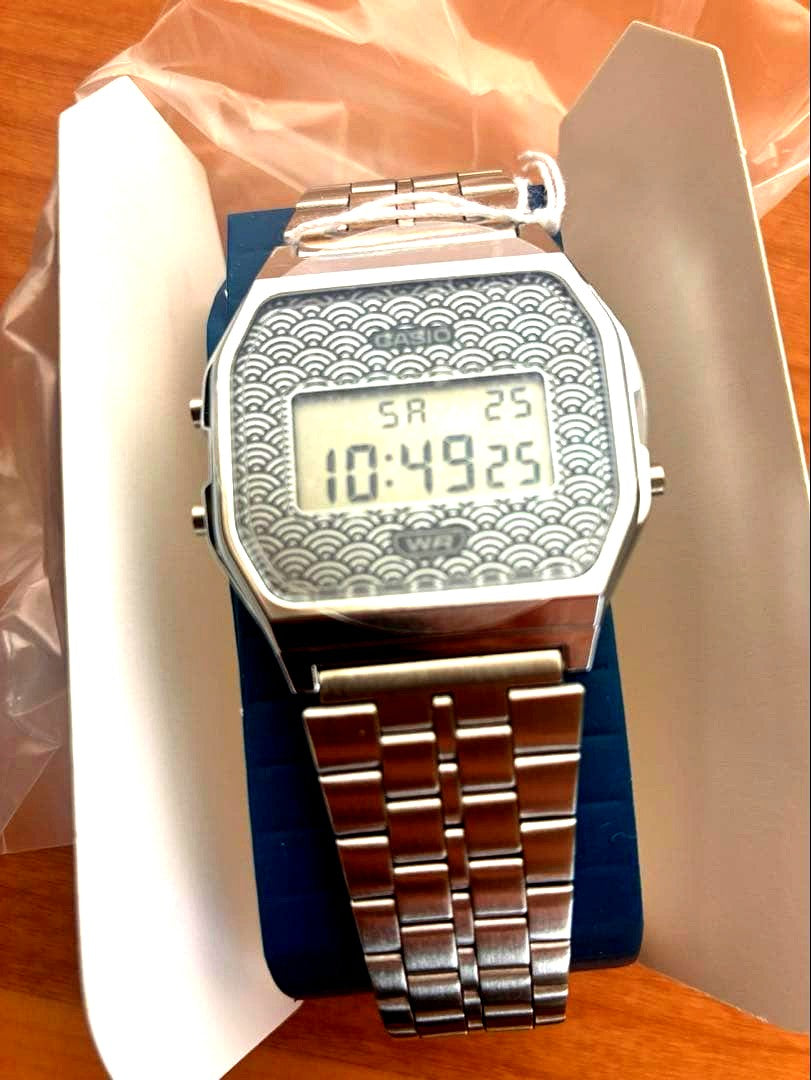 Casio A168WE-1 digital watch with silver wave pattern dial and stainless steel band, displayed with box and tags