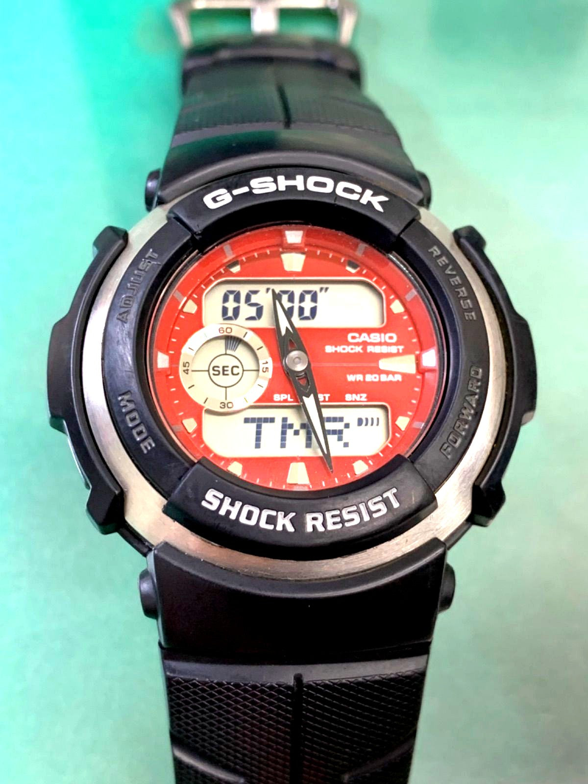 Casio G-300 digital watch with red dial and battery movement showing analog and digital displays